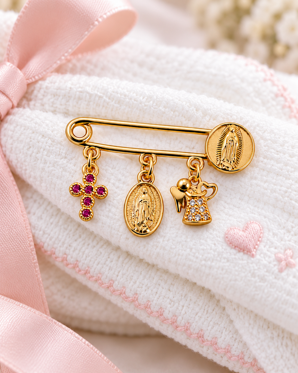 Pink cross baby blessing pin with Our Lady of Guadalupe medals and angel charm on a pink and white blanket