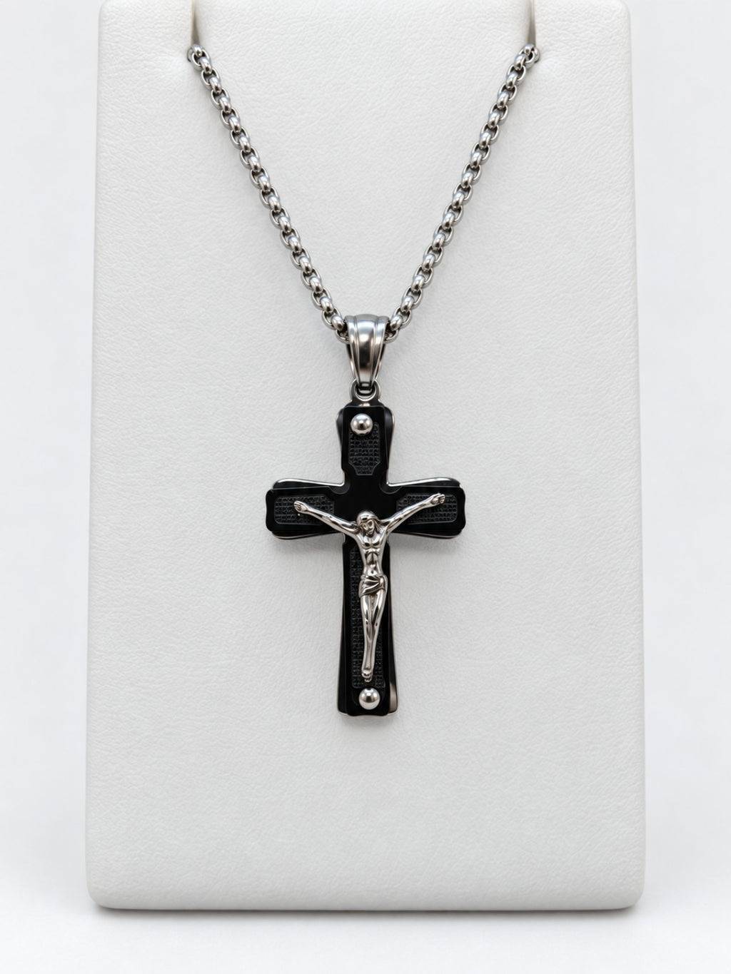 A black crucifix with dark textured panels, a raised silver-tone figure of Jesus and silver-tone chain.