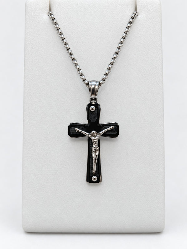 A black crucifix with dark textured panels, a raised silver-tone figure of Jesus and silver-tone chain.