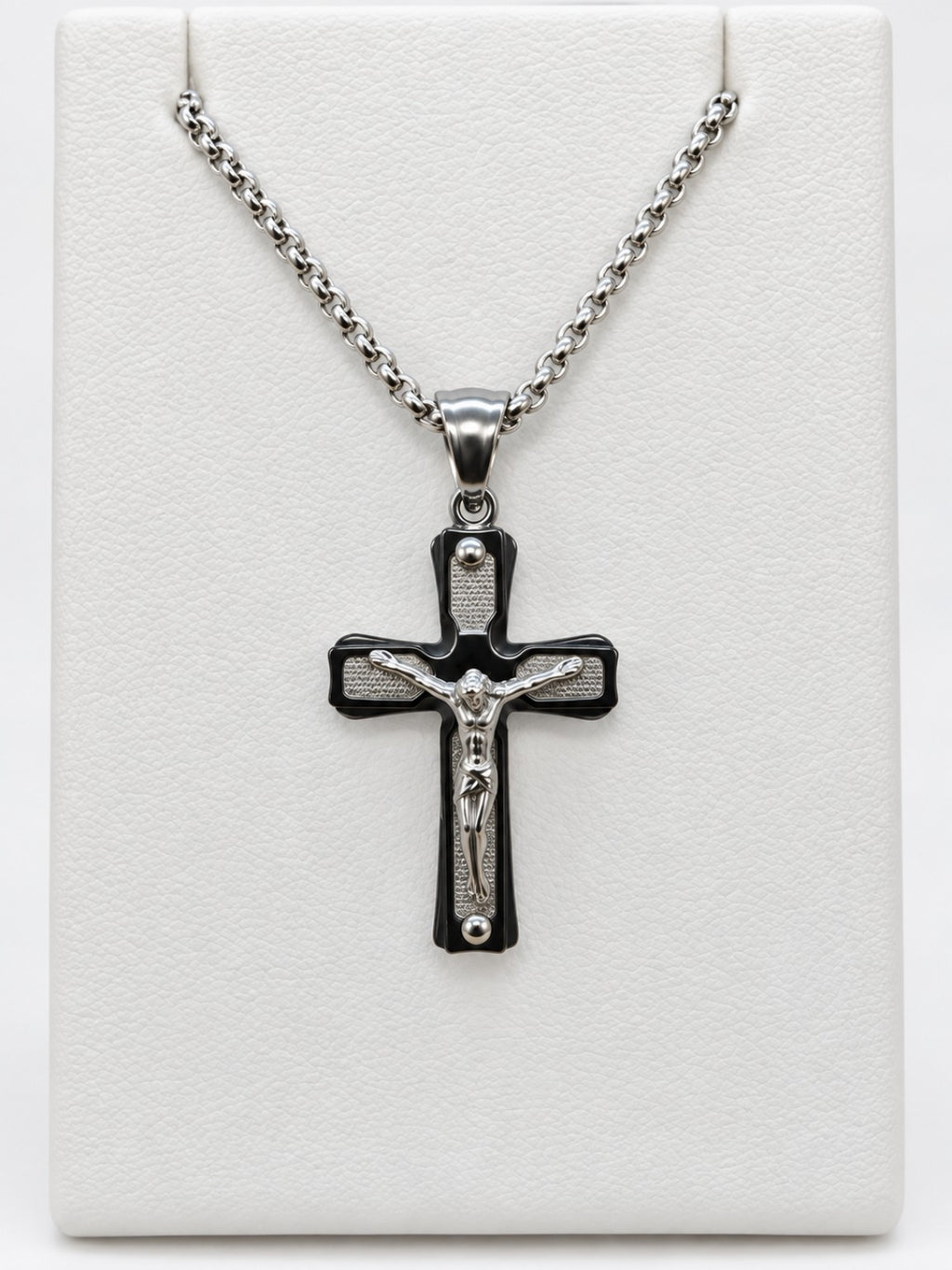 A crucifix with silver-tone textured panels, a dark border, a raised silver-tone figure of Jesus and silver-tone chain.